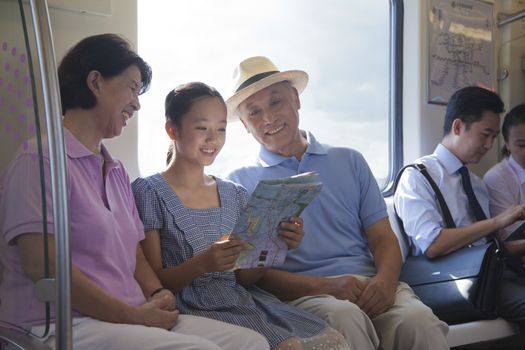 Granddaughter with grandparents sitting in the subway and looking at the map