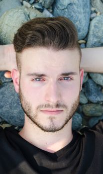 Portrait of attractive young man resting on rocks, looking in camera