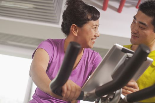 Woman smiling and exercising on the exercise bike with her trainer
