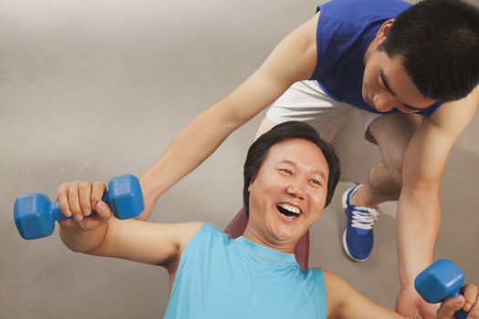 Mature man working out with weights, trainer supporting him