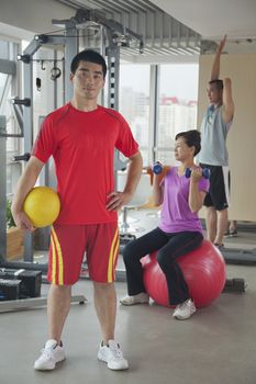 Young man holding ball in the gym, people working out on the background