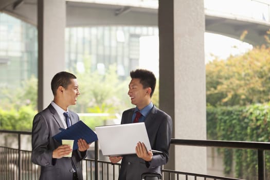 Two young businessmen working outdoor, looking at each other 