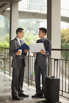 Two young businessmen working outdoor, looking at each other 