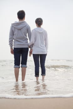 Young couple standing on the beach and looking out to sea     