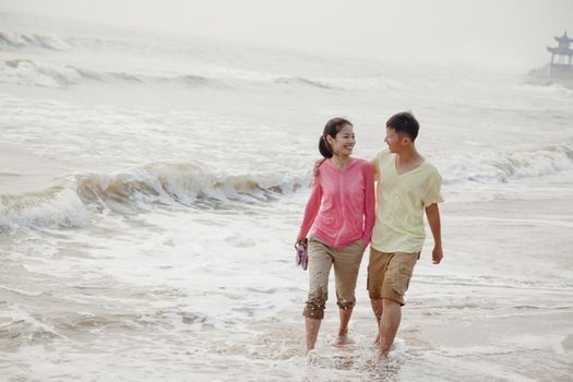 Young couple walking by the waters edge on the beach, China