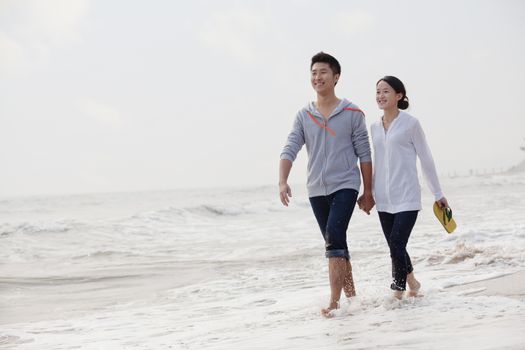 Young couple walking by the waters edge on the beach, China