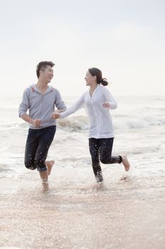 Young couple holding hands and running by the waters edge on the beach, China