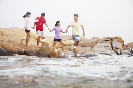 Four friends walking over rocks by the sea