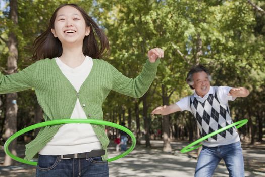 Granddaughter with grandfather playing with plastic hoop in the park