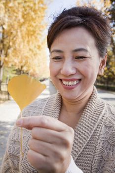 Mature Woman Holding Yellow Ginkgo Leaf