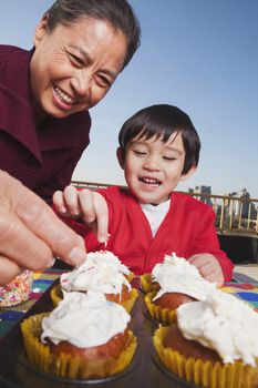 Grandmother and grandson decorating cupcakes