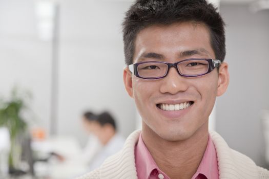 Businessman smiling in the office, coworkers in the background