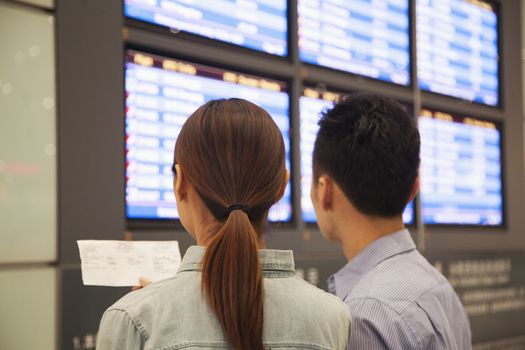 Two travelers looking at flight departure screens at airport
