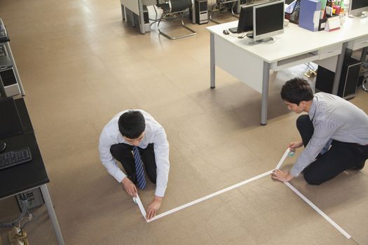 Two young businessmen taping up the floor in the office