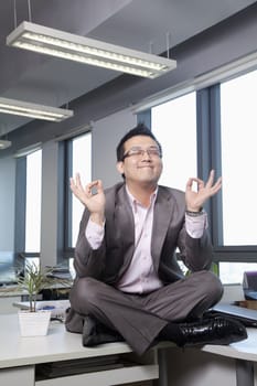 Businessman sitting on desk in the office meditating 