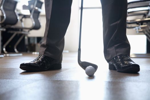 Businessman playing golf in his office, close up on feet 