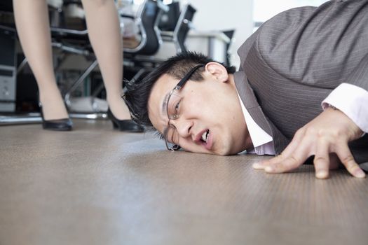 Businessman with face on the floor, coworker standing by him