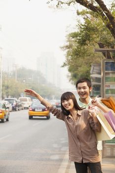 Young couple with shopping bags hailing a taxicab in Beijing