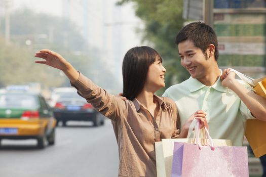 Young couple looking at each other with shopping bags hailing a taxicab in Beijing