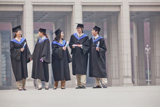 Five Graduate Students Standing and Talking With Diplomas