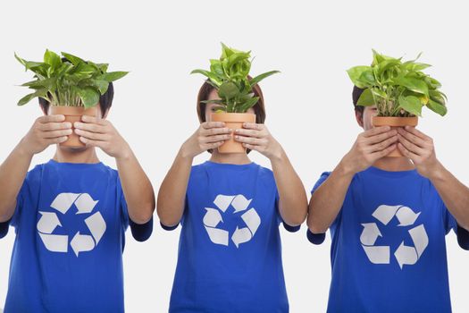 Three people holding plants, obscuring faces, studio shot