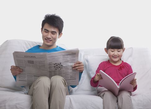 Father and daughter sitting on sofa reading separately, studio shot