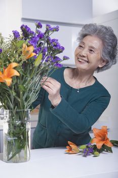 Senior Woman Looking and Touching a Bouquet of Flowers in the Kitchen