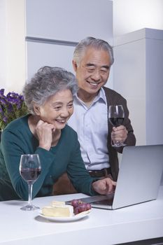 Mature Couple Looking at Laptop in the Kitchen, Drinking Wine 