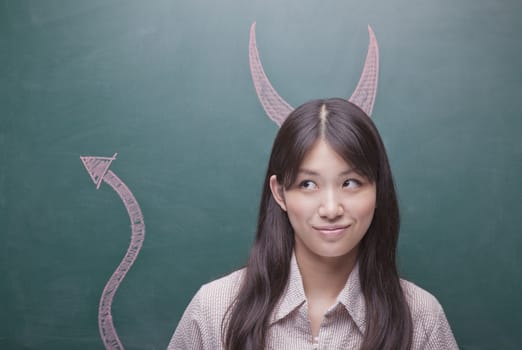 Young woman with devil horns and tail on blackboard