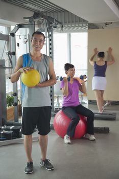 Mature man holding ball in the gym, people exercising on the background