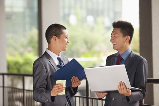 Two young businessmen working outdoor, looking at each other  