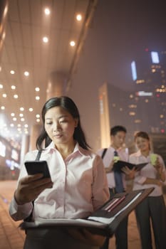 Young businesswoman with her cell phone, coworkers on the background, portrait