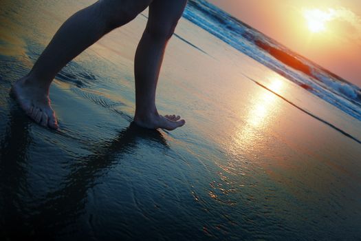 Male legs walking throught the beach during sunset. Artistic darkness and colors added