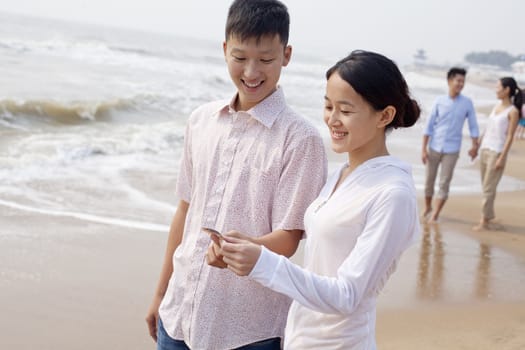 Young couple standing and looking at seashell on the beach, China