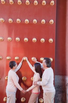 Granddaughter with grandparents standing next to the traditional red doors and holding hands