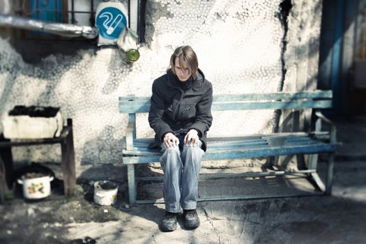 Sad man sitting on the bench at special smoking place. Shallow depth of field due to the tilt/shift lens for movie effect