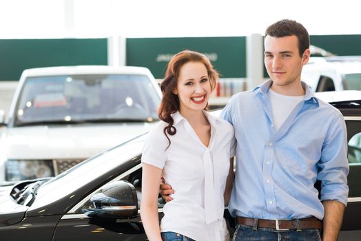 Young couple standing embracing near a car in the showroom