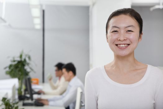 Businesswoman smiling in the office, coworkers in the background