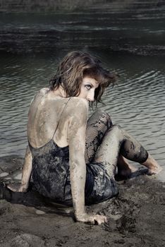 Backview on a woman with dried dirty on her skin sitting at the beach