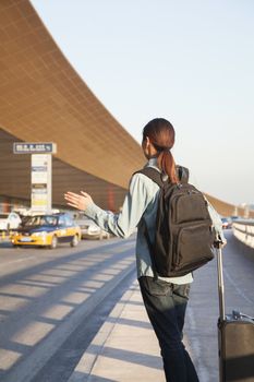 Young traveler hailing a taxi at airport