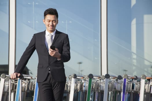 Traveler looking at cellphone next to row of luggage carts