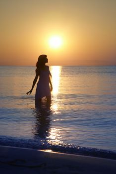 Silhouette of the serene woman standing in the water during golden sunset. Natural colors and darkness