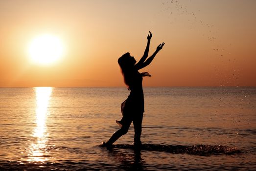 Silhouette of the woman playing with water splashes during golden sunset