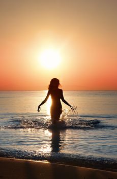 Silhouette of the woman walking in the water during beautiful sunrise. Natural light and darkness. Artistic vivid colors added