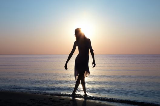 Silhouette of the lady standing at the beach during sunset. Sunlight is going through woman's hair. Natural light and colors