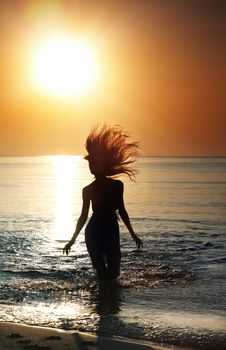 Silhouette of the woman with long hairs running in the sea during golden sunset. Natural darkness and colors. Vartical photo