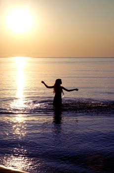 Silhouette of the woman playing with water during sunset. Natural darkness and colors