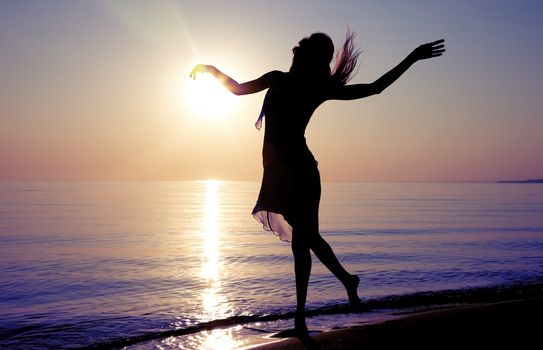 Silhouette of the woman dancing at the beach during beautiful sunrise. Natural light and darkness