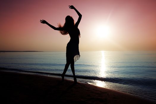 Silhouette of elegant lady dancing at the beach during sunset