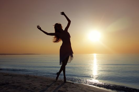 Silouette of the nifty woman dancing at the sea during sunset. Natural light and darkness. Artistic colors added